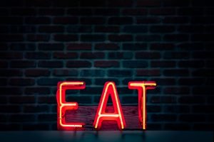 Ein rotes Neonlicht zeigt das Wort „EAT“ vor einer dunklen Backsteinwand. Die strahlenden Buchstaben symbolisieren Essensreize, die auch bei ADHS Schweiz eine Rolle im Umgang mit impulsivem Essverhalten spielen können.