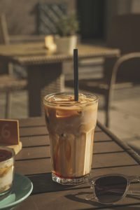 Ein Glas Eiskaffee mit Strohhalm steht auf einem Holztisch in der Sonne, daneben eine Sonnenbrille. Gerade bei ADHS Schweiz spielt der bewusste Konsum von koffeinhaltigen Getränken eine wichtige Rolle für den Tagesrhythmus.